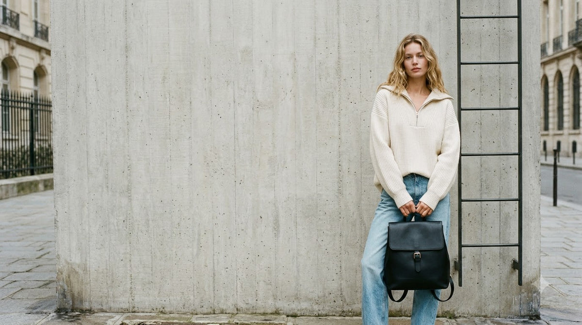 Model holding a black leather backpack against a concrete wall